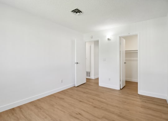 A room with white walls and wooden flooring with two open doors.