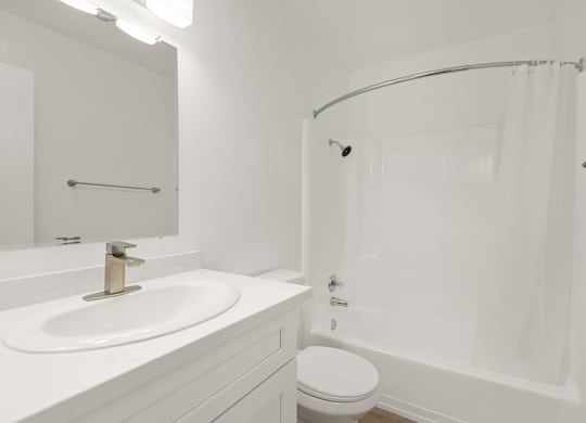 A white bathroom with a sink, toilet, and shower.
