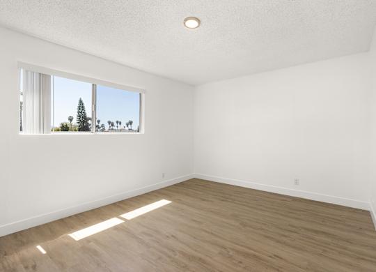 Empty room with wooden floor and a window showing a tree outside.