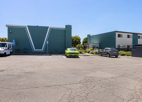 A green car is parked in front of a grey building.