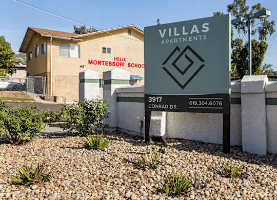 A sign for Villas Apartments stands in front of a building with a Montessori school.