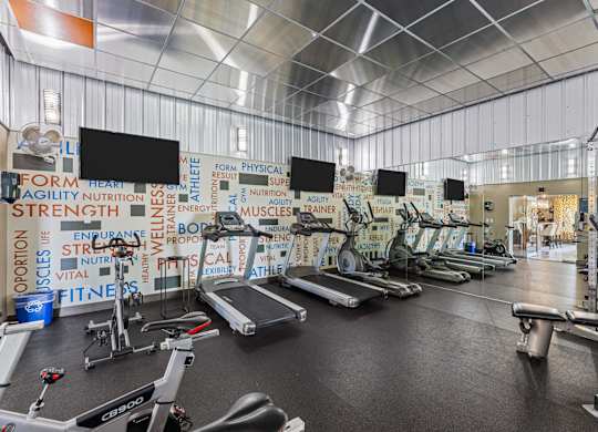 A gym with a variety of equipment and a wall covered in fitness related words.