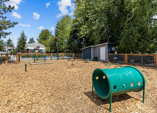 A playground with a green tube slide and a brown wooden fence.