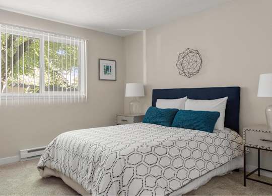 A bedroom with a large bed and a window with blinds.