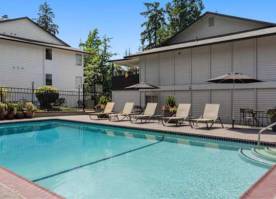 A pool with chairs and umbrellas in front of a house.