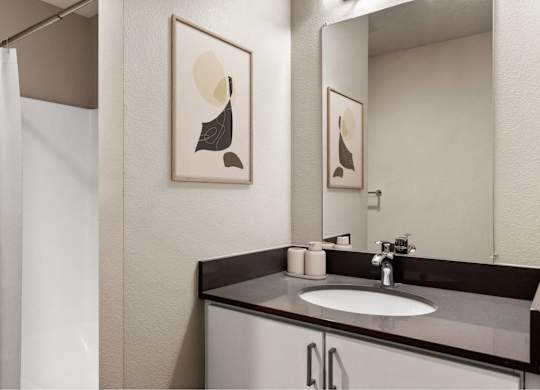 A bathroom with a sink, mirror, and two framed pictures on the wall.