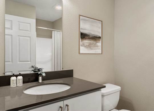 A bathroom with a sink, toilet, and a painting on the wall.