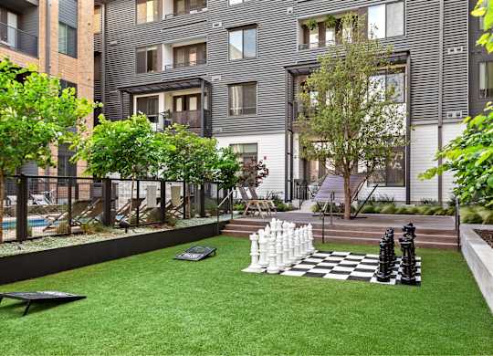 A chess set sits on a green lawn in front of a building.