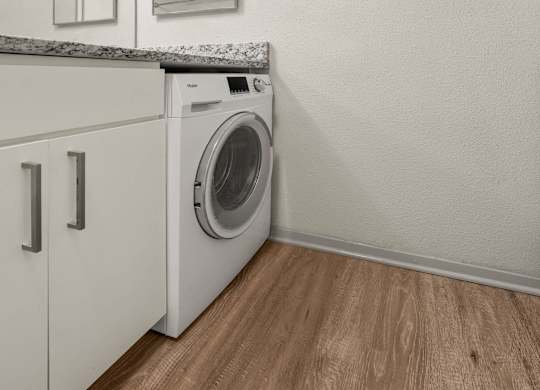 A white washing machine in a laundry room with wooden flooring.