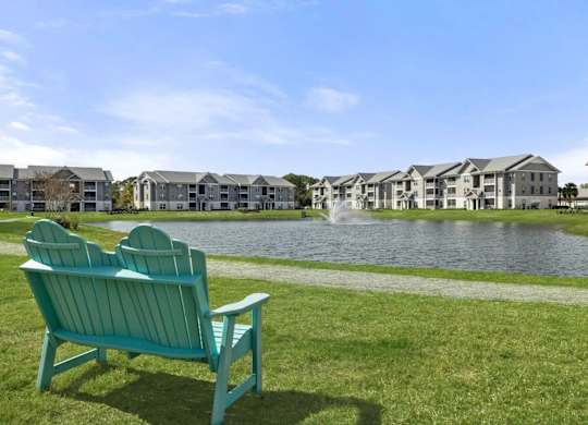 Two blue chairs are on a lawn in front of apartment buildings.