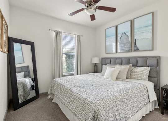 A bedroom with a large bed, a ceiling fan, and a view of a beach through the windows.