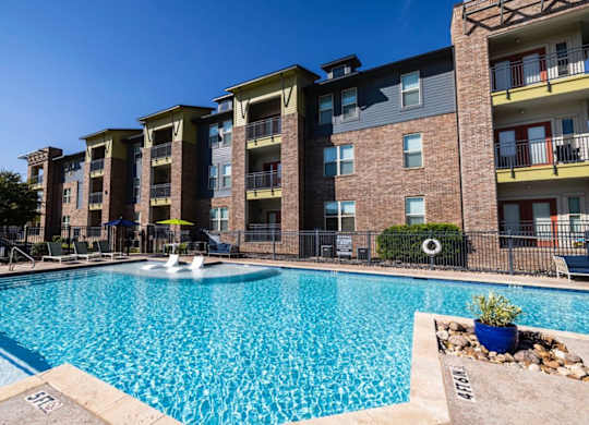 A large swimming pool in front of a multi-story apartment building.