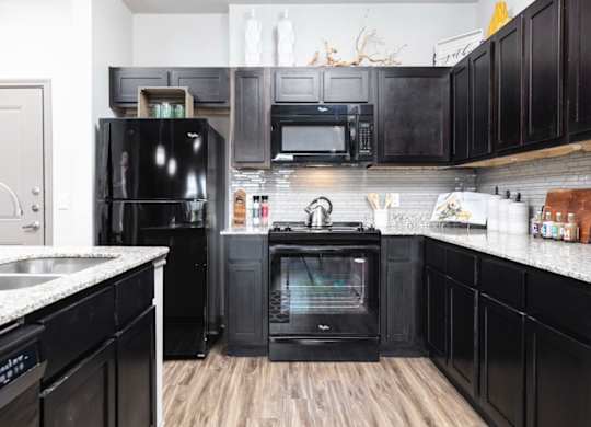 A black fridge and oven in a kitchen with wooden floors.