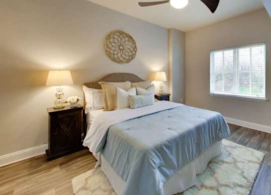 A bedroom with a bed, two lamps, a ceiling fan, and a window.