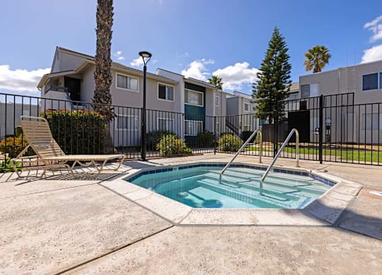 A pool surrounded by a black fence with a chair and a tree in the background.