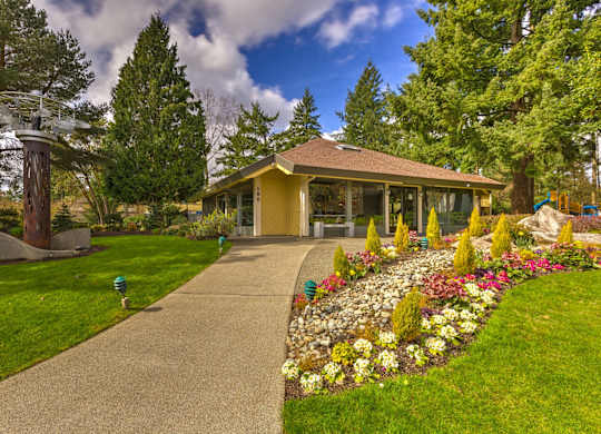 A yellow building with a brown roof is surrounded by a garden with a variety of flowers.