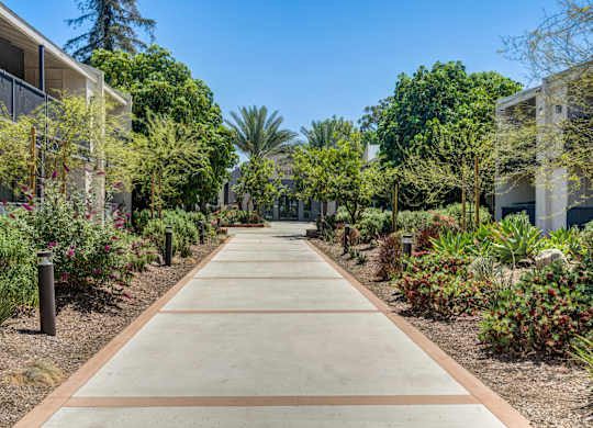 A long concrete pathway leads through a landscaped area with trees and shrubs on either side.