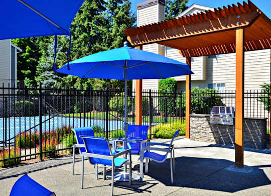 A blue umbrella is on a patio with a pool in the background.