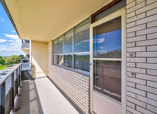 A balcony with a brick wall and a window overlooking a tree-filled landscape.