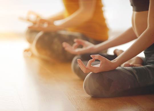 Two people are sitting cross-legged on the floor in a meditative pose.