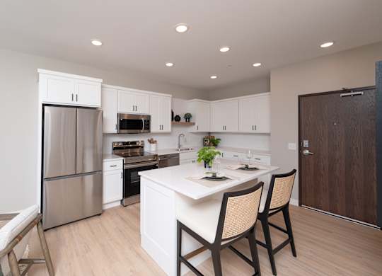 A kitchen with a white island and wooden chairs.
