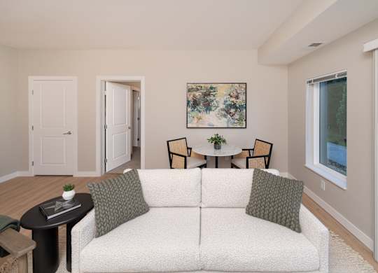 A living room with a white couch and a painting on the wall.