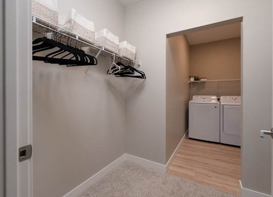 A white closet with clothes hanging and a laundry room in the background.