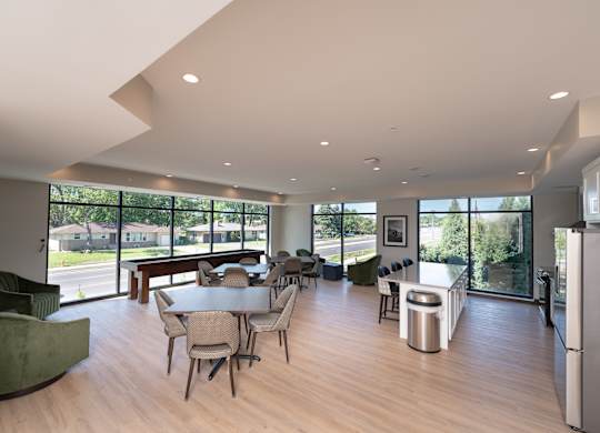 A modern community room kitchen with a dining table, comfortable chairs and shuffle board game.