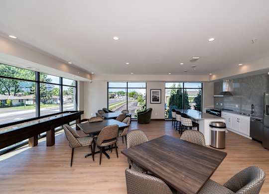 A modern community room kitchen with a dining table, comfortable chairs and shuffle board game.