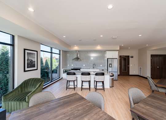 A modern community room kitchen with a dining table, comfortable chairs and shuffle board game.