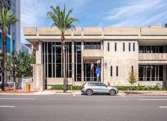 A silver car is parked in front of a concrete building with palm trees.