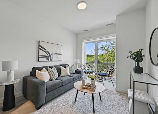 A living room with a grey couch, a round table, and a large window at Roxy Apartments, Hamilton