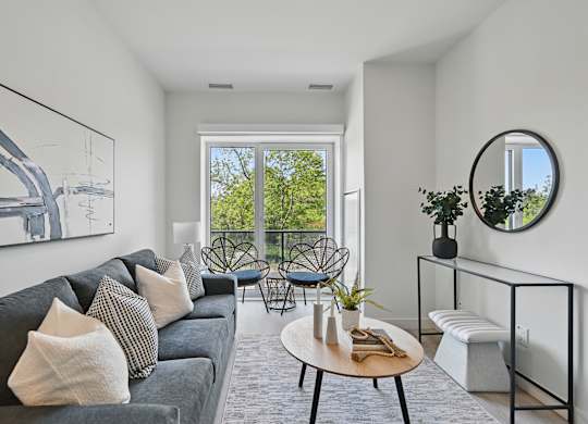 A living room with a grey couch and a round mirror on the wall at Roxy Apartments, Hamilton, ON