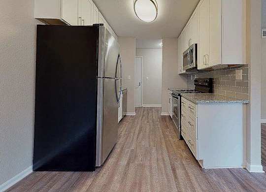 A black refrigerator is in the corner of a kitchen with wood flooring. at Spalding Vue, Peachtree Corners, 30092