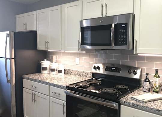 A kitchen with a black stove top oven and a black microwave above it. at Vue on Medlock, Peachtree Corners, Georgia