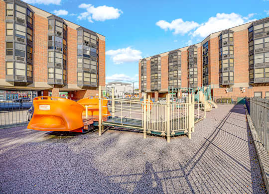 A playground area in front of a building with orange and grey buildings in the background at Fullerton Court Apartments, Chicago, 60614