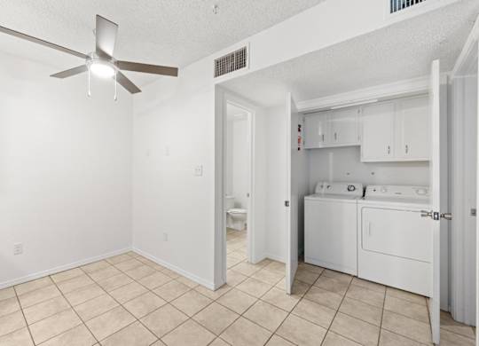 A white room with a fan and a bathroom with a toilet and sink.