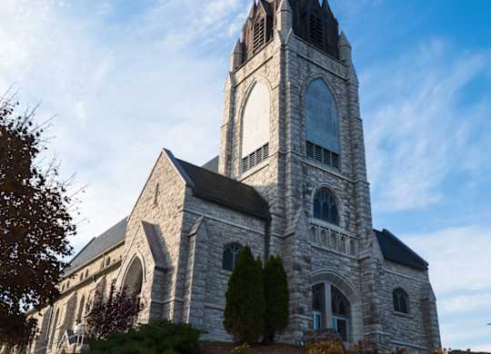 A church with a tall steeple and a cross on top stands against a blue sky at The Grove Apartments, Orillia, L3V 1H4