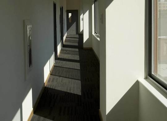 A long hallway with carpeted floors and windows on the side.at 66 Main, Yonkers, NY 10701