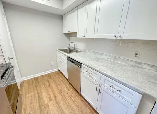A kitchen with white cabinets and a marble countertop.