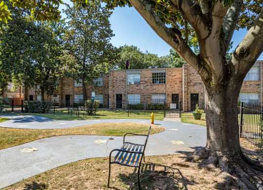 A playground with a bench and a tree in front of a brick building.