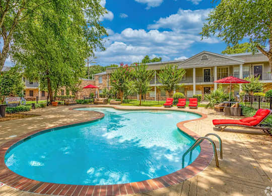 A swimming pool surrounded by a red brick border with a building in the background.