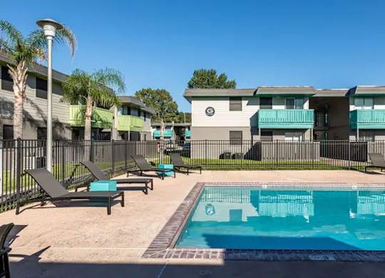 A swimming pool is surrounded by sun loungers and palm trees.