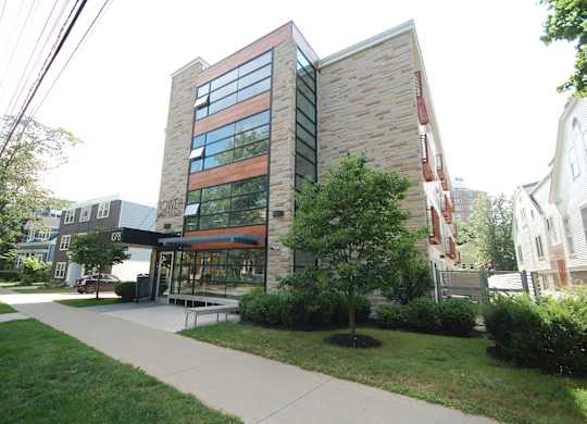 A modern building with a glass facade is surrounded by greenery and a sidewalk.