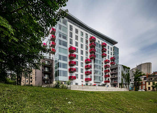 A modern building with red balconies is surrounded by greenery.