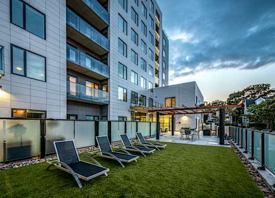 A modern building with a glass facade and a small garden area with lounge chairs.
