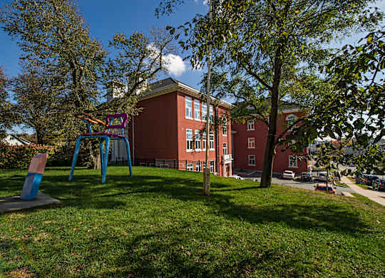 A playground with a swing set in front of a red building.