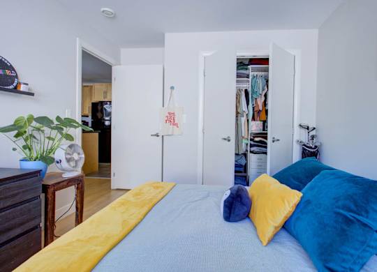 A bed with a yellow blanket and blue pillows is in the foreground of a room.