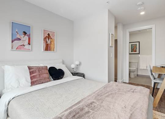 A bedroom with a bed, two pillows, a nightstand, a chair, and a painting on the wall.