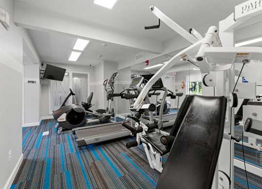 A gym with a variety of equipment including a treadmill, rowing machine and weights.